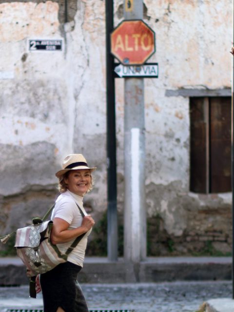 Nerys Parry turning back to smile at the camera on a cobbled street in Antigua, Guatemala, a backpack over one shoulder and an ALTO stop sign behind her