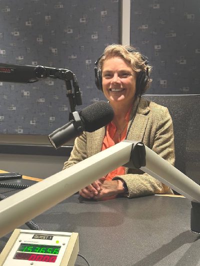 Nerys Parry in a radio studio, wearing headphones and smiling behind a broadcast microphone