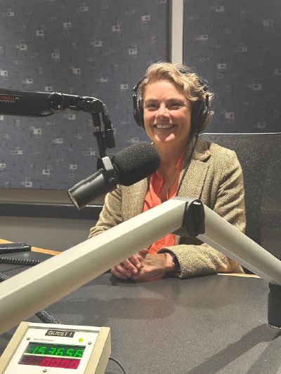 Nerys Parry in a radio studio, wearing headphones and smiling behind a broadcast microphone